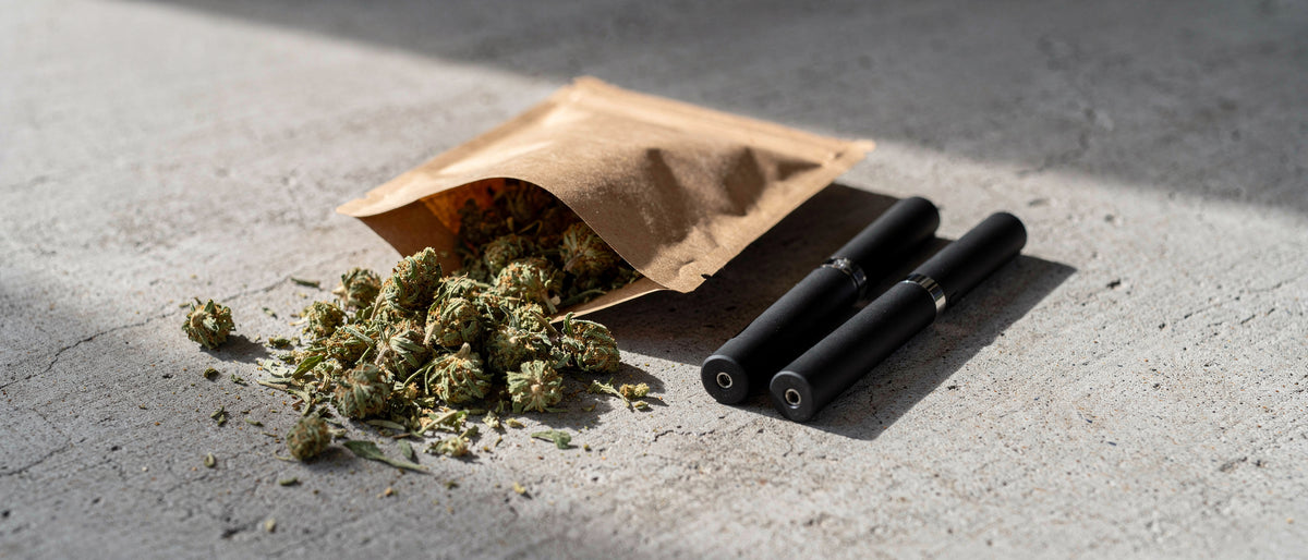 Kraftpapier-Beutel mit Hanfblüten und zwei schwarze Einweg-Vapes auf Beton im Tageslicht, Symbolbild zu Superior Blend Erfahrungen