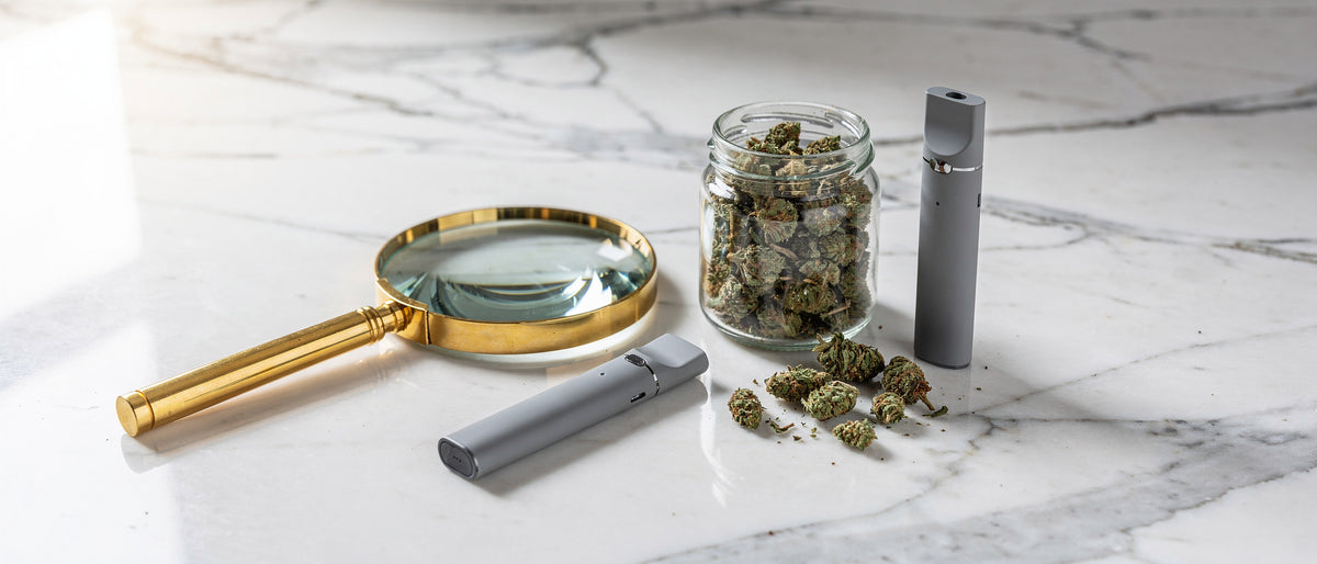 Lupe, Glas mit Hanfblüten und zwei graue Einweg-Vapes auf weißem Marmor im Tageslicht, Symbolbild zur Frage Ist Superior Blend legal