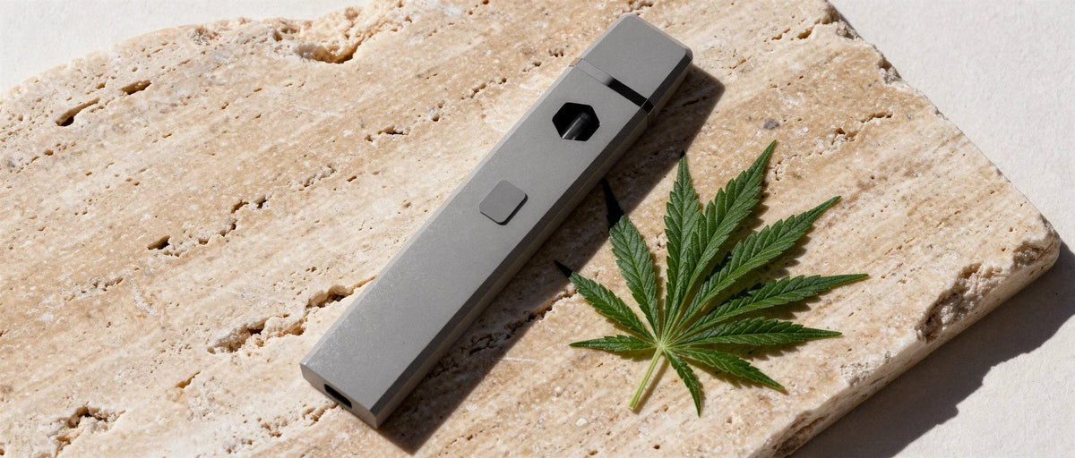 Graue Einweg-Vape neben einem Hanfblatt auf Travertin, CBD Vape Wirkung