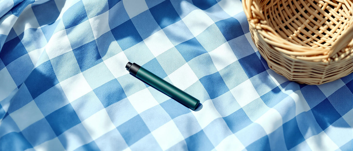 Dunkelgrüner Einweg-Vape auf Picknickdecke neben Weidenkorb im Tageslicht, Symbolbild DNT-9 Erfahrungen