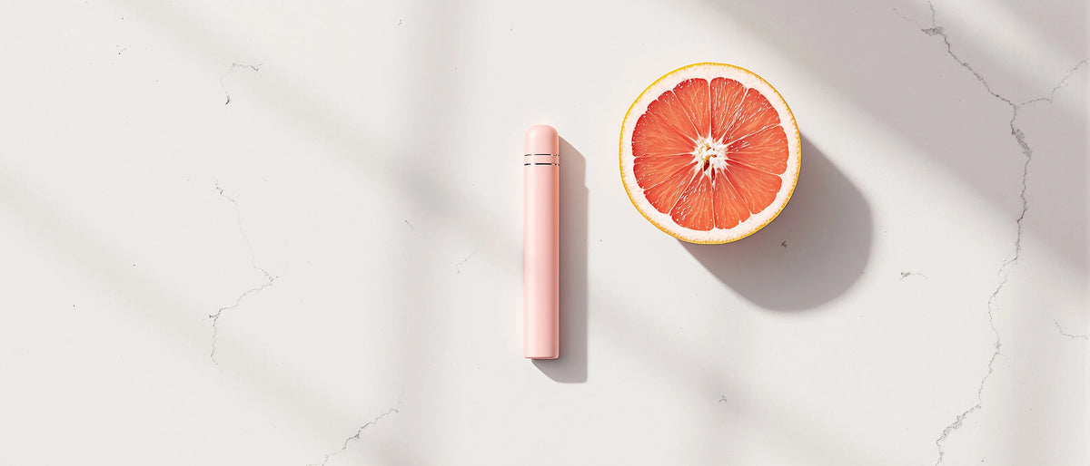 Rosa Einweg-Vape neben halbierter Grapefruit auf weißem Marmor im Tageslicht, Symbolbild H4CBD Wirkung
