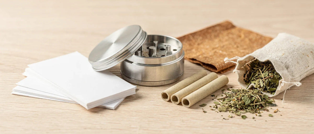 Metall-Grinder, weiße Papers, Filter-Tips, Hanf-Wrap und Kräutermischung auf hellem Holz, Thema Joint, Blunt, Spliff Unterschied