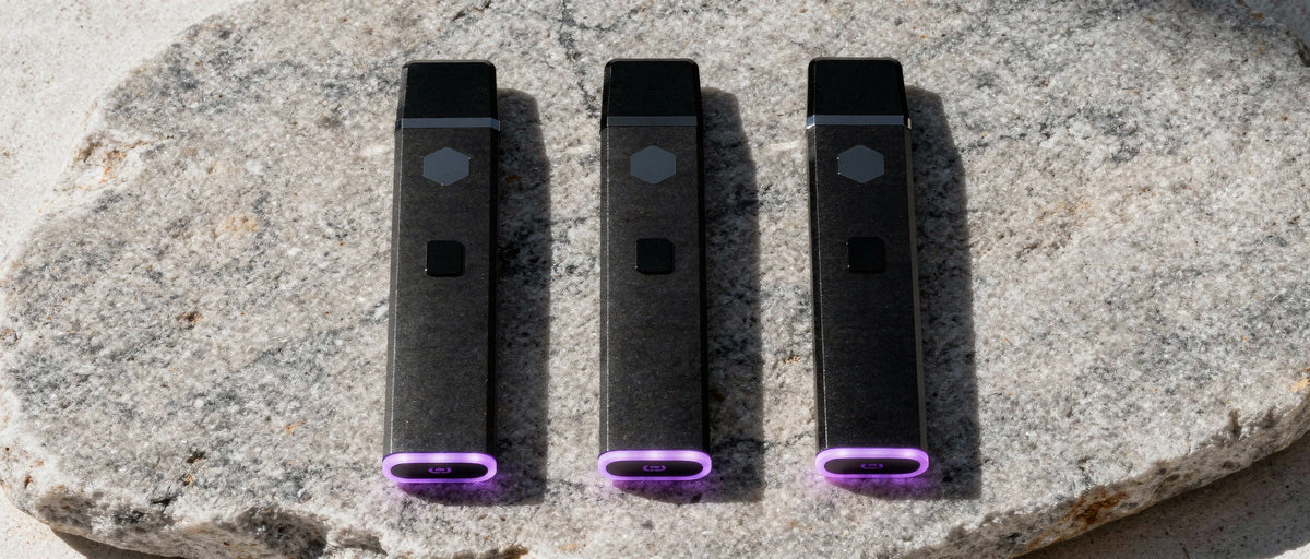 Drei schwarze Einweg-Vapes mit violettem Leuchtring auf hellem Naturstein, Thema Meshflash Erfahrungen
